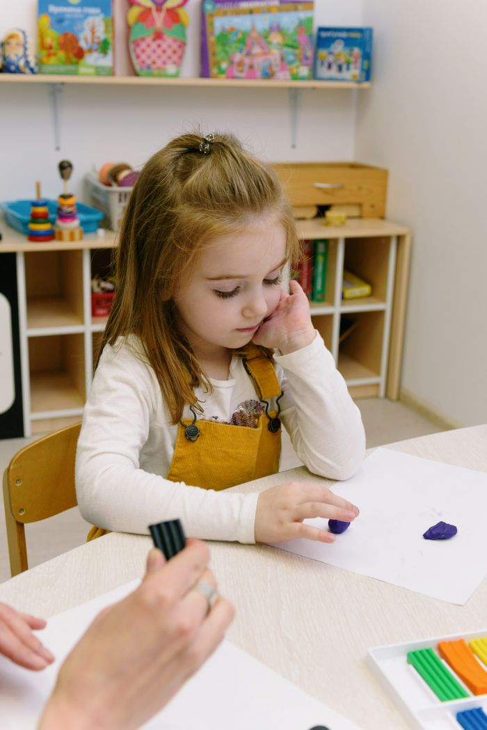 A young girl is engaged in creative play with modeling clay in a kindergarten setting.